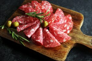 Salami with green olives on a wooden dish